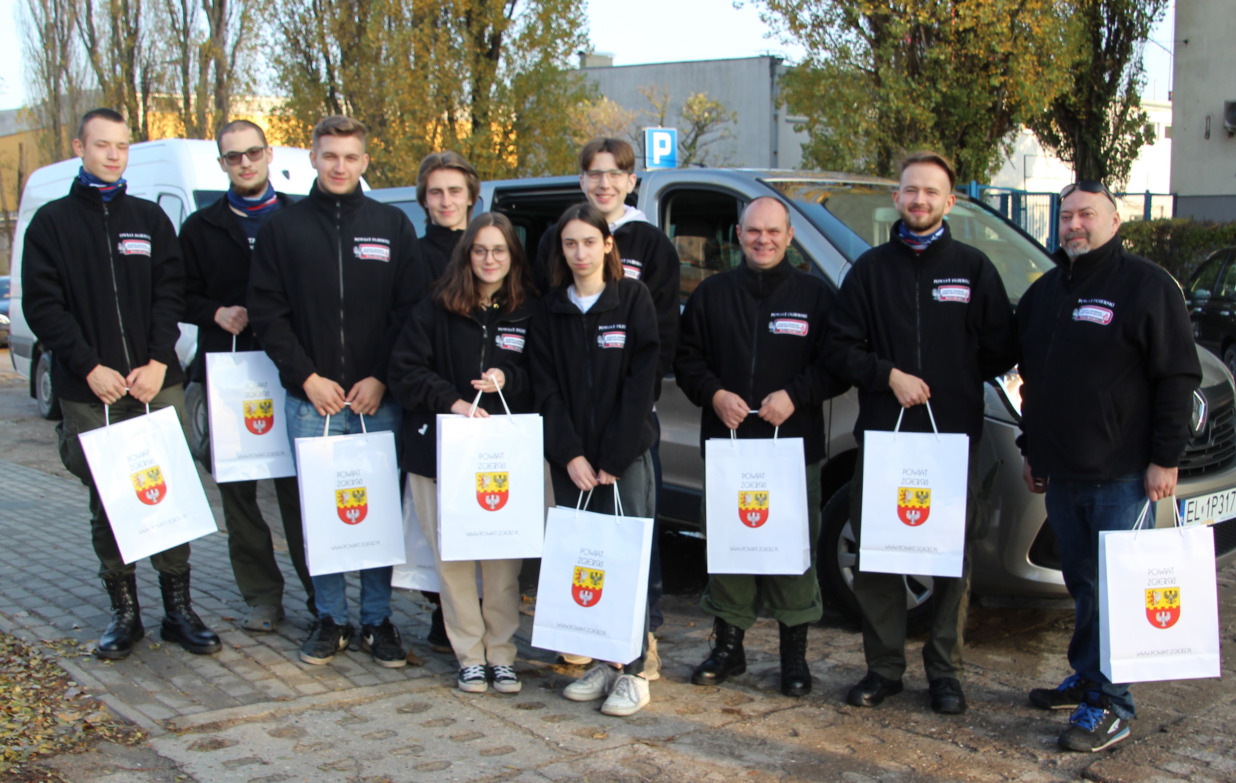 Grupa harcerzy przed budynkiem starostwa, pozują do zdjecia z torbami z gadżetami przekazanymi przez Powiat Zgierski