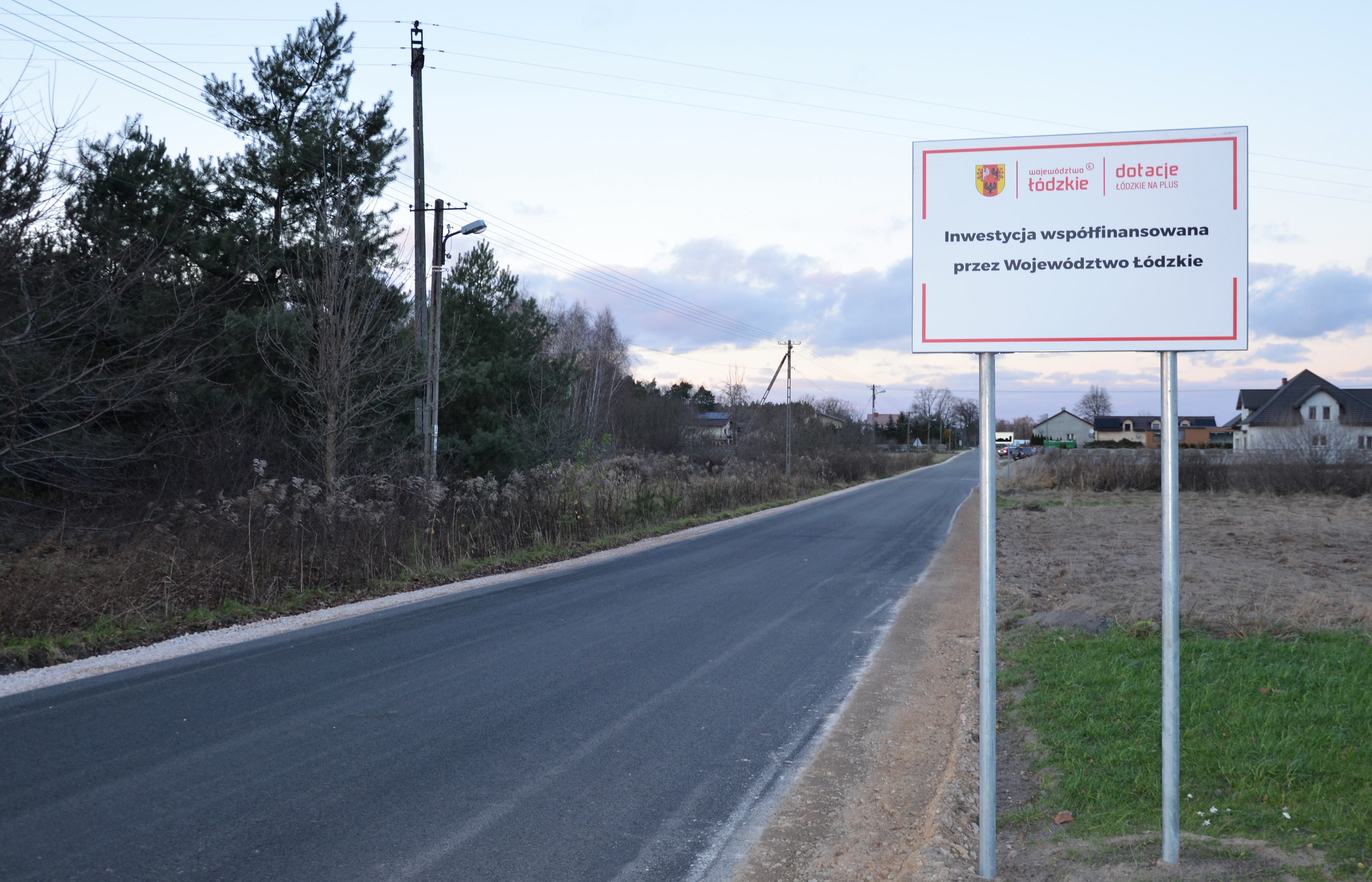 Wyremontowana droga, obok niej znajduje sie tablica informująca o udziale samorządu wojewódzkiego w inwestycji