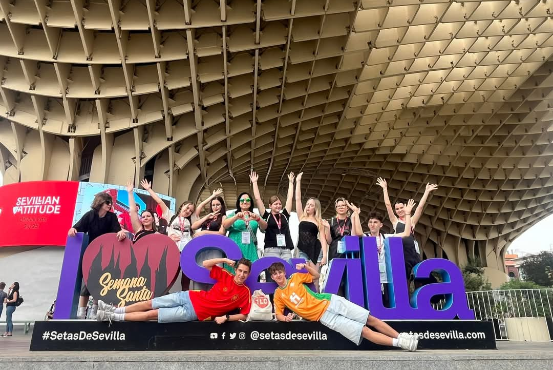 Grupa młodzieży pozuje przy dużym fioletowym napisie Sevilla