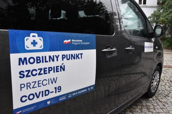 Szczepieniobus - zdjęcie boku ciemnego busa, opatrzonego naklejką z napisem: mobilny punkt szczepień przeciw COVID-19