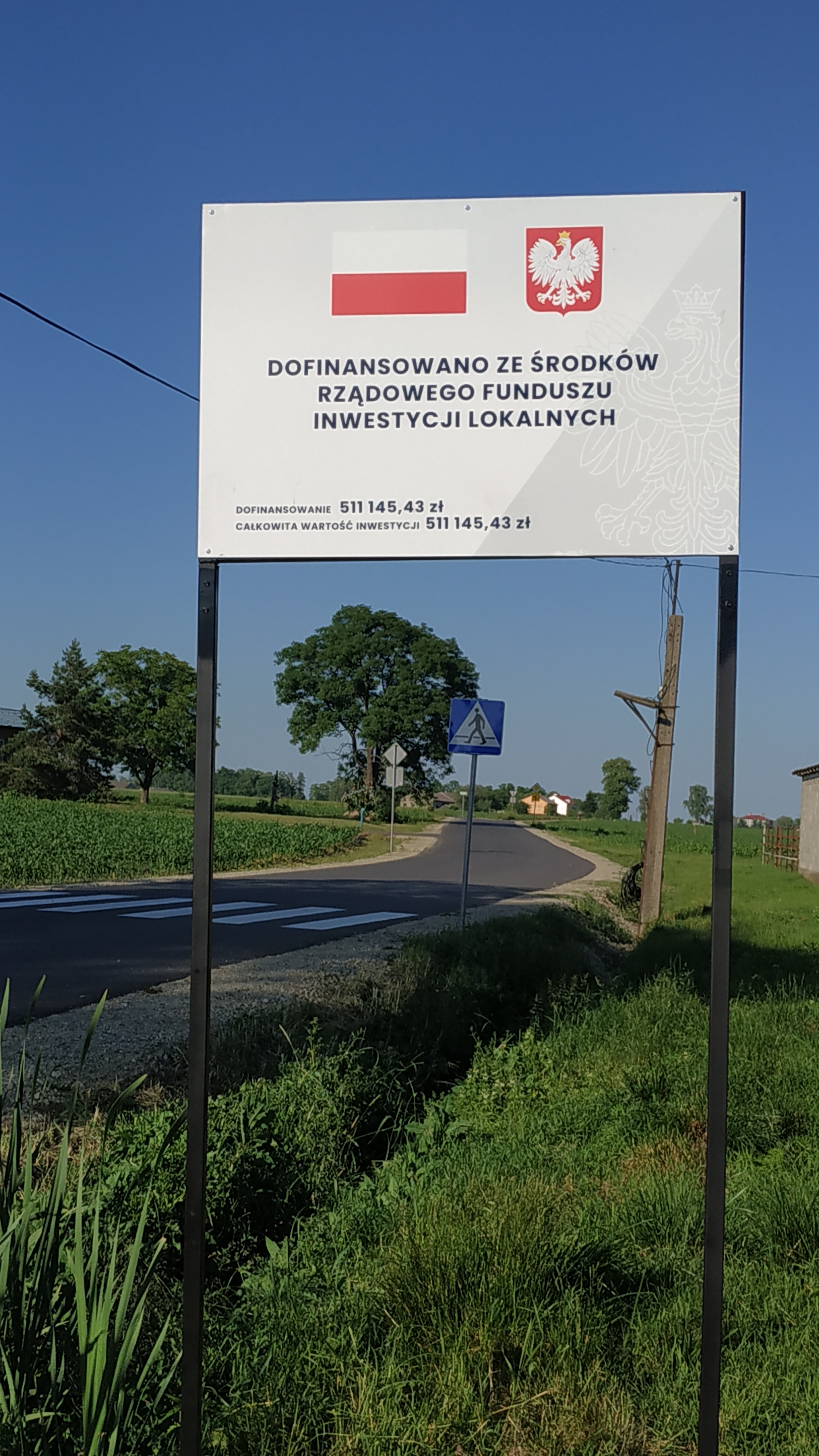 Zdjęcie przedstawia drogę wraz z tablicą informacyjną od strony m. Popów Głowieński